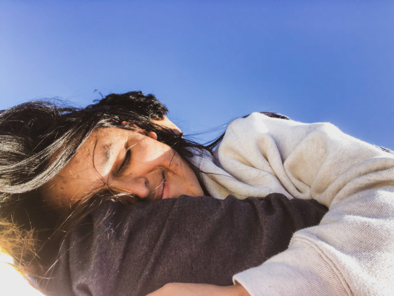 cozy warm couple cuddled at the beach, girl wrapped around boys arm, boys face is hidden, girl is smiling with eyes closed